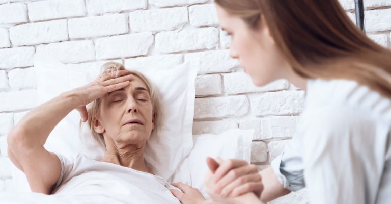 daughter holds elderly mothers hand who requires overnight care