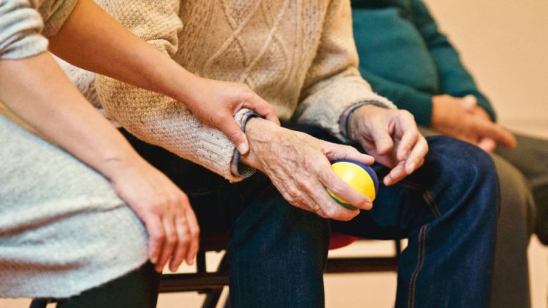 Elderly man holds ball whilst family members hold his hand