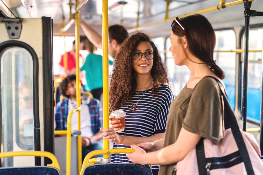 Two girls standing in a bus chatting and drinking coffee.